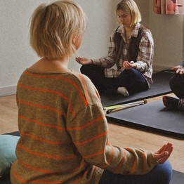 Personen entspannen im Schneidersitz auf Yogamatten