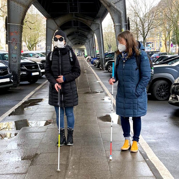 Eine Teilnehmerin befindet sich mit Frau Kaufmann im Orientierung- und Mobilitätstraining mit dem Langstock