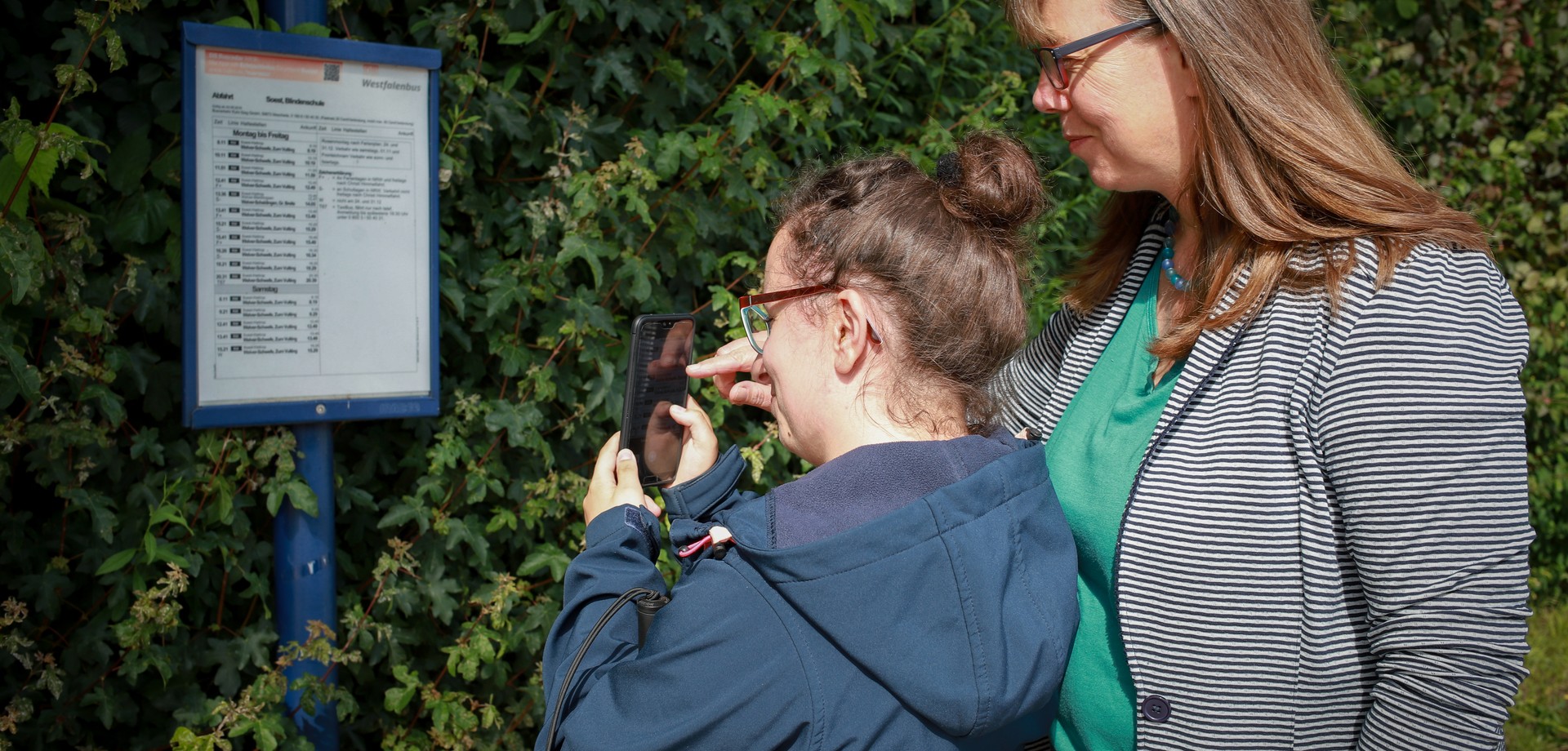 Zwei Personen gehen mit einem Smartphone einen Busfahrplan durch