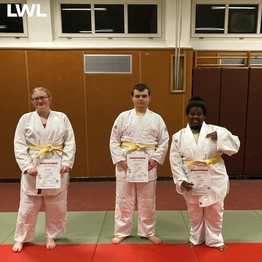 Die drei Judoka posieren auf der Matte mit ihren neuen Gürteln