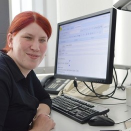Maren Hesse sitzt an ihrem Arbeitsplatz und lächelt in die Kamera