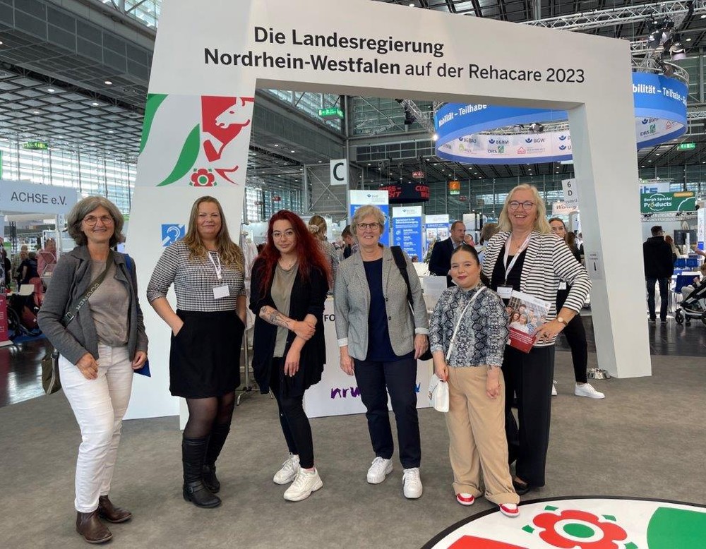 Die Teilnehmerinnen mit Frau Oeser und Frau Sauerland vor dem Stand vom Ministerium für Arbeit, Gesundheit und Soziales der Landesregierung